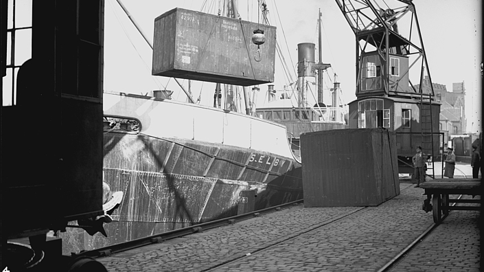 Ein schwarzweiß Foto vom Hamburger Hafen, auf dem zu sehen ist, wie ein sogenannter Liftvan verladen wird.