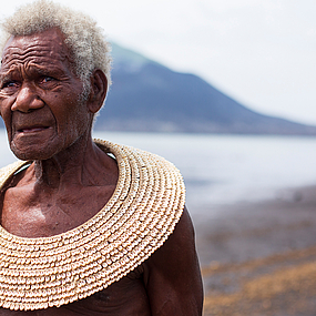 Eine Frau mit traditionellem Schmuck aus Papua New Guinea vor einer Bergkulisse.