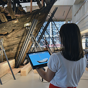 Frau mit Tablet steht vor der Kogge.