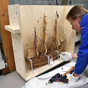 Ein Museumsmitarbeiter packt ein Schiffsmodell ein.