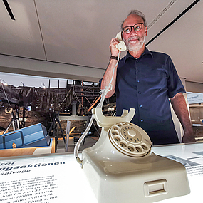 Der Vermittler Bernd Wecker hält einen Telefonhörer in der Hand.